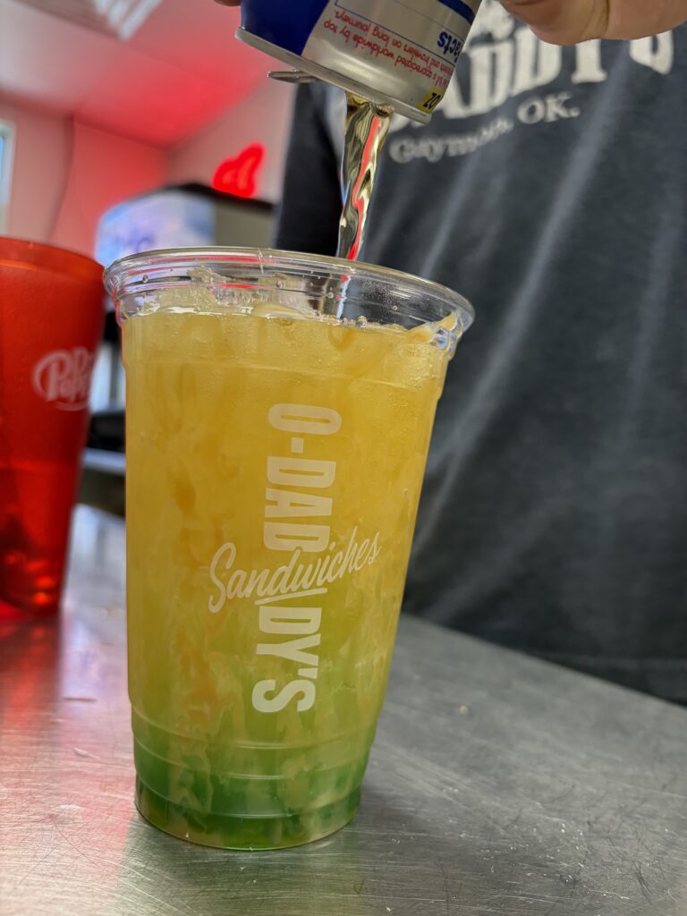 Red Bull Energy Drink Poured Into a Clear Branded O-Daddy's Cup Filled with Crushed Ice and Layered Flavor Syrup | O-Daddy's Brick Oven Sandwiches